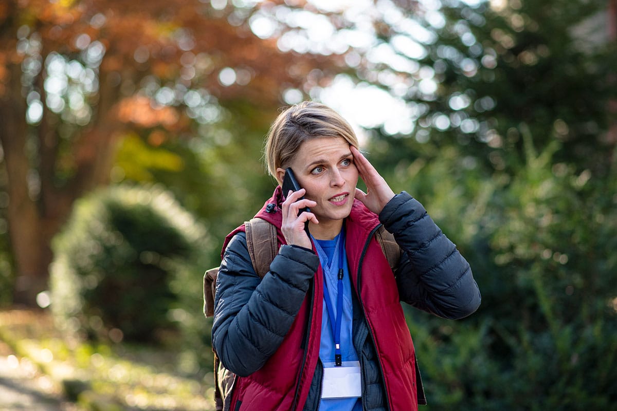 female nurse in a red vest is holding her head and calling in sick to work because of a headache