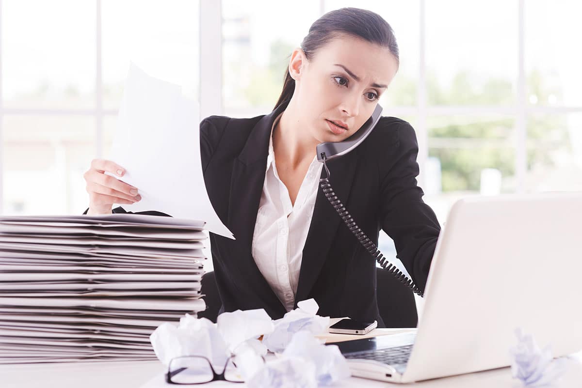 women in suit sitting at her desk which is swamped with paperwork