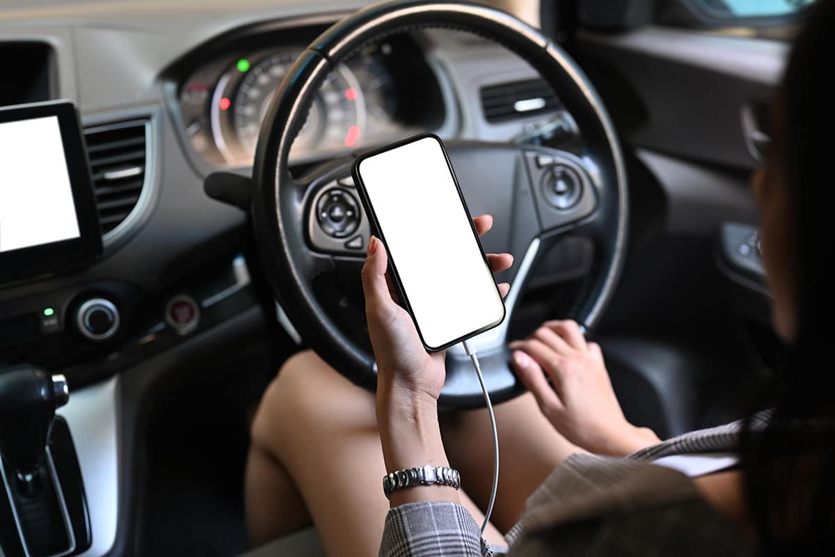 women in a car holding her cell phone but not driving