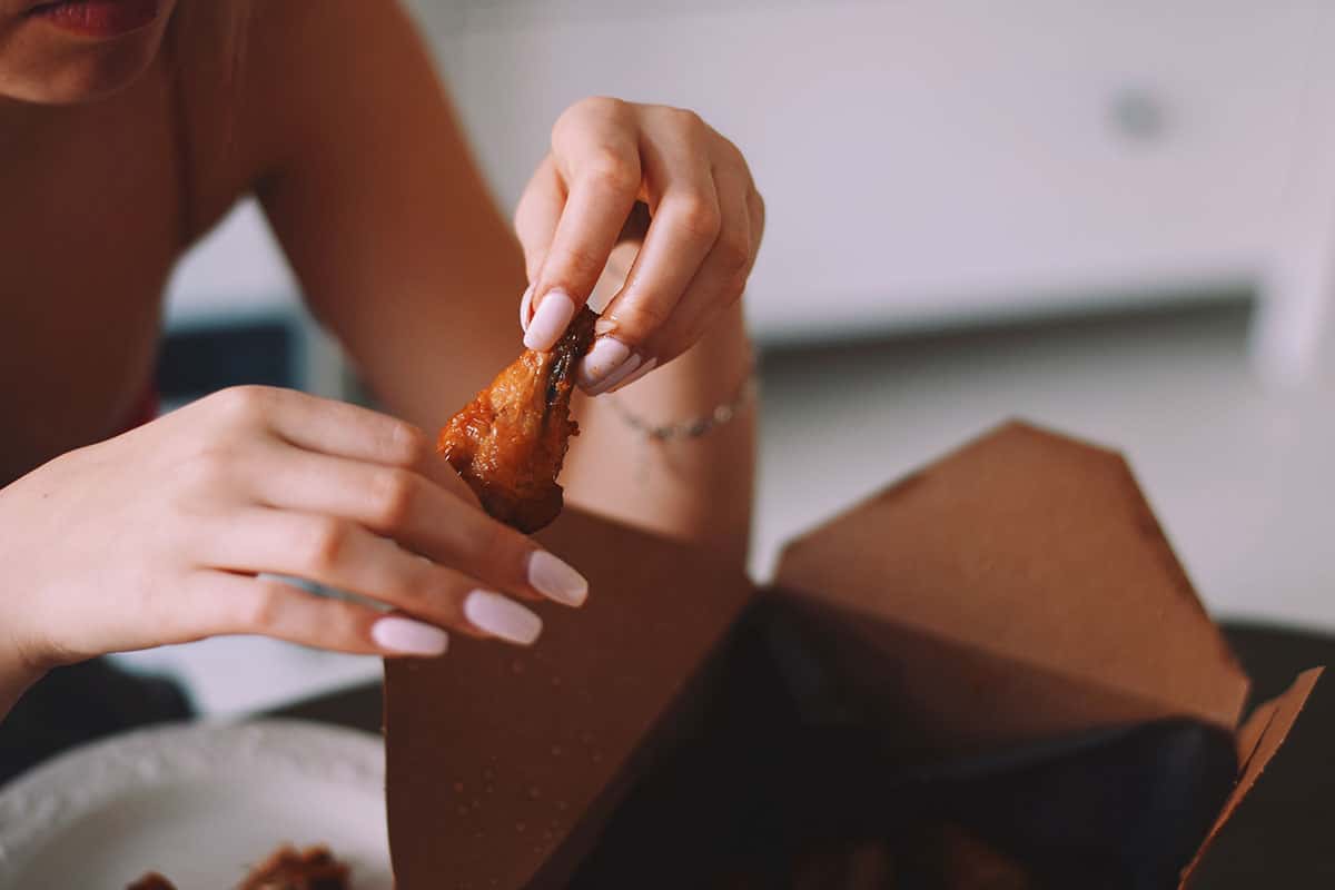 woman with pink nails picking up a chicken wing