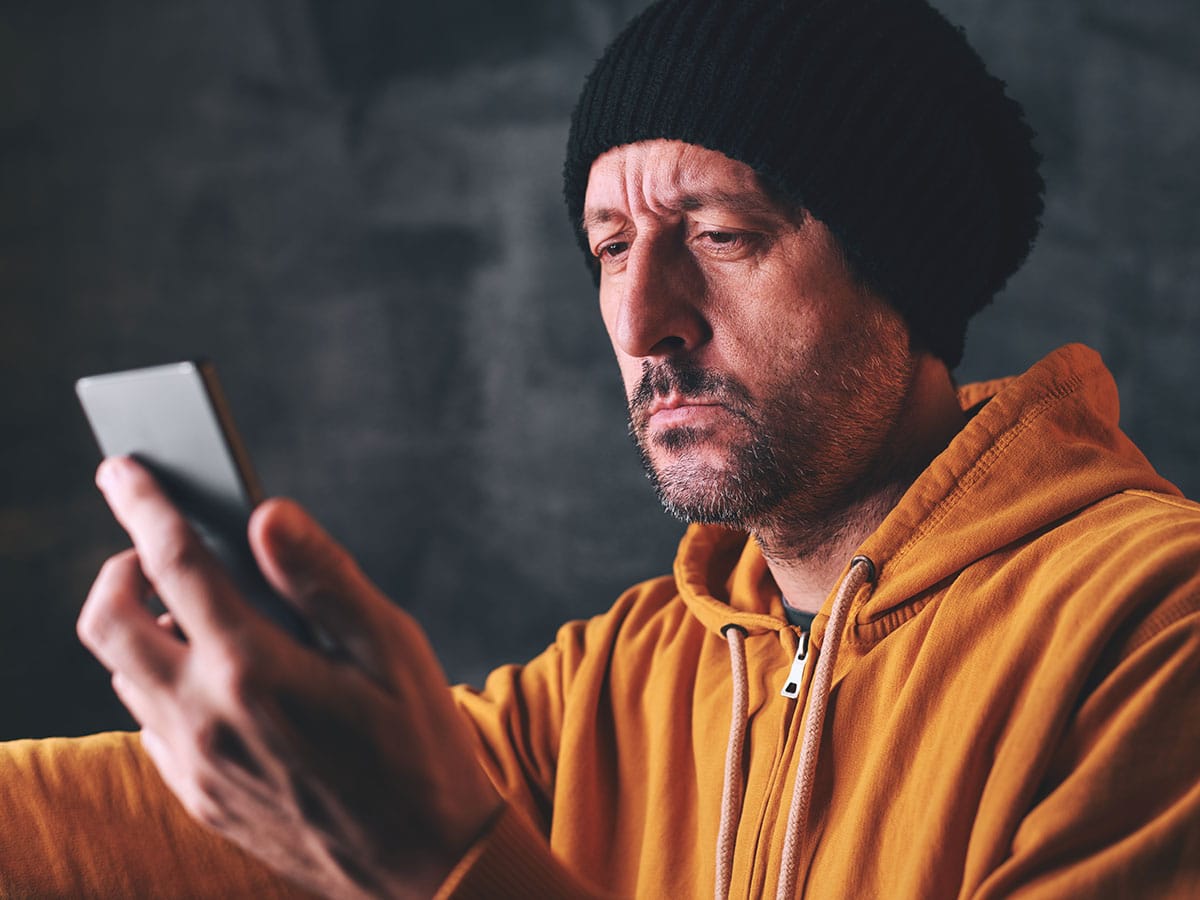 man in orange sweater and black beanie looking at sad with his phone