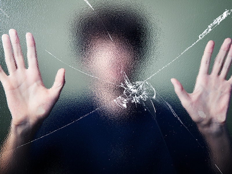 man holding his hands up against a broken window