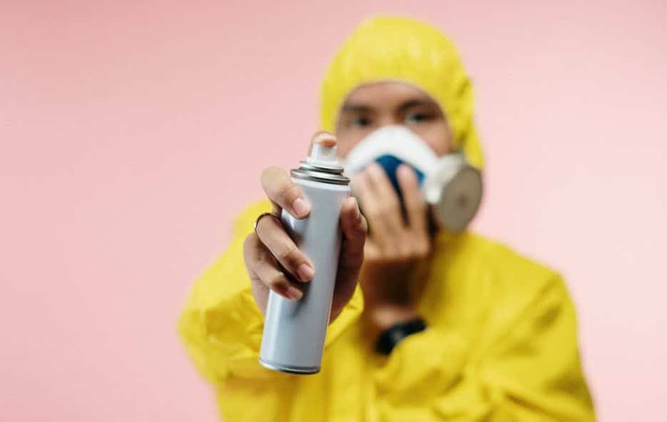 man in a yellow exterminator suit spraying an aerosol can