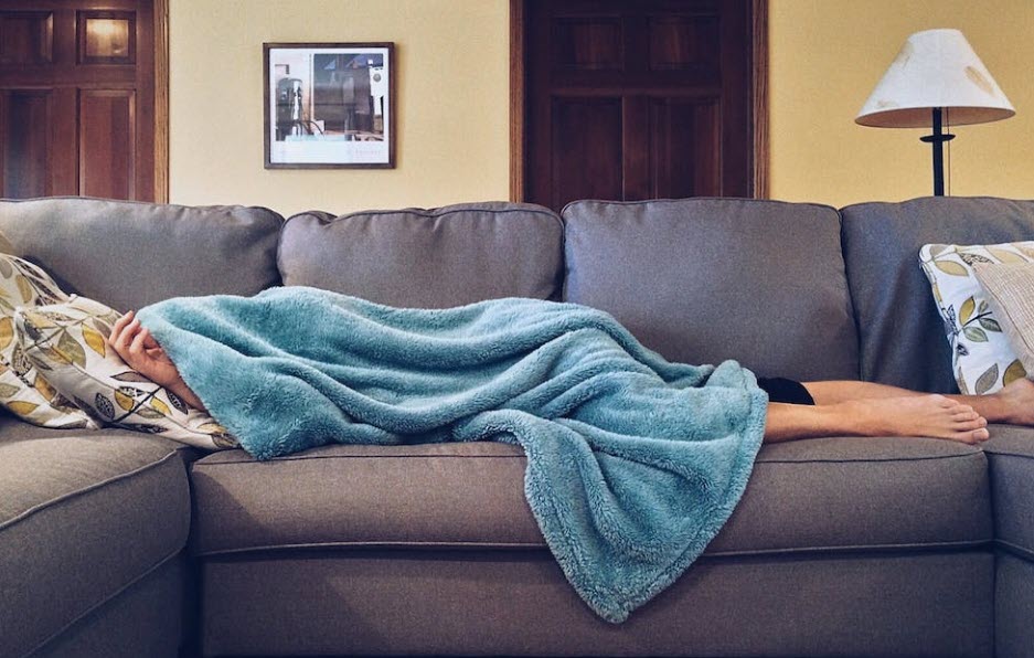 tired guy on couch with a blanket covering him