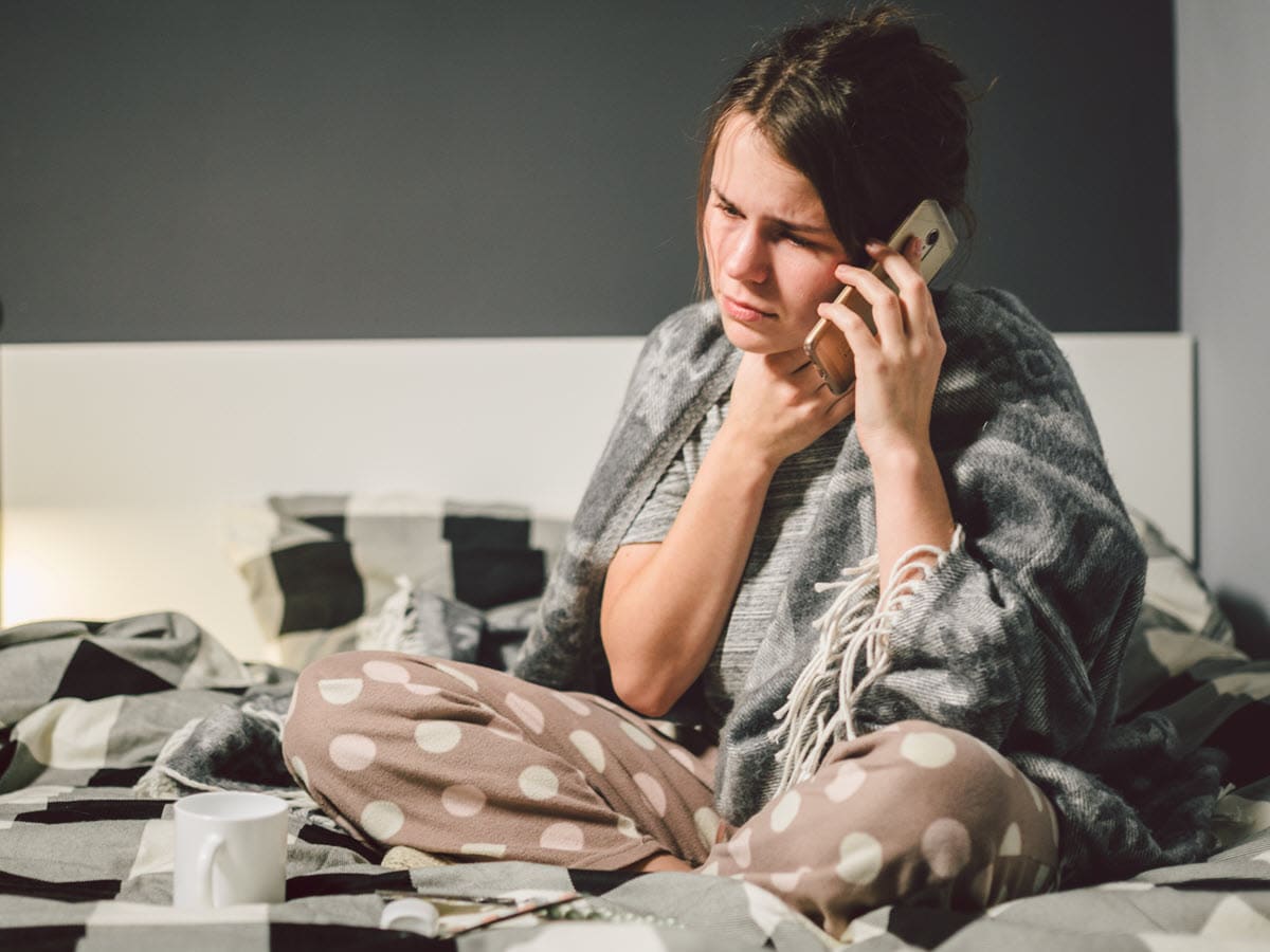 woman in bed calling in sick to work