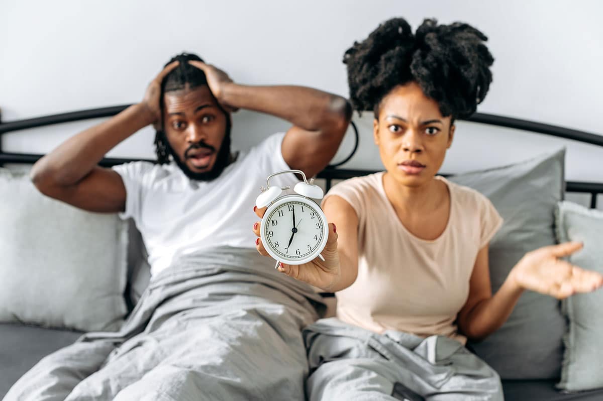 couple still in bed totally shocked because they overslept and are now late for a wedding reception