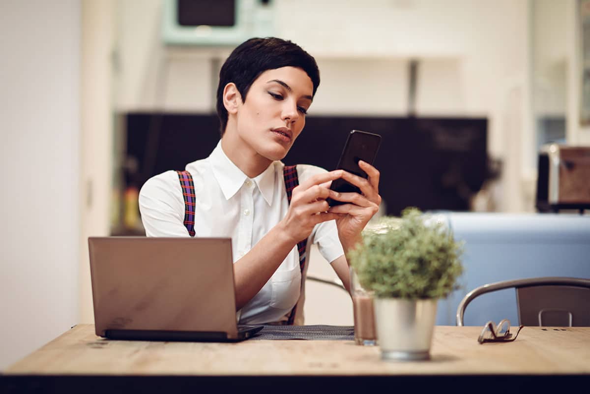 business woman with a short haircut sitting at her desk answering email son her phone