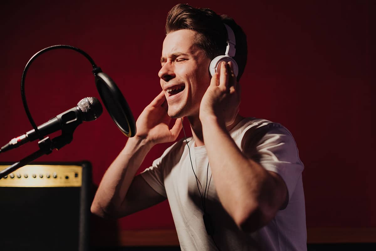 young man in a recording booth singing into a microphone while wearing headphones