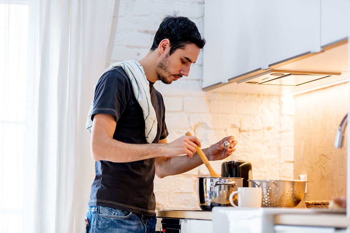 man in black trshirt stands over the stove salting some pasta water