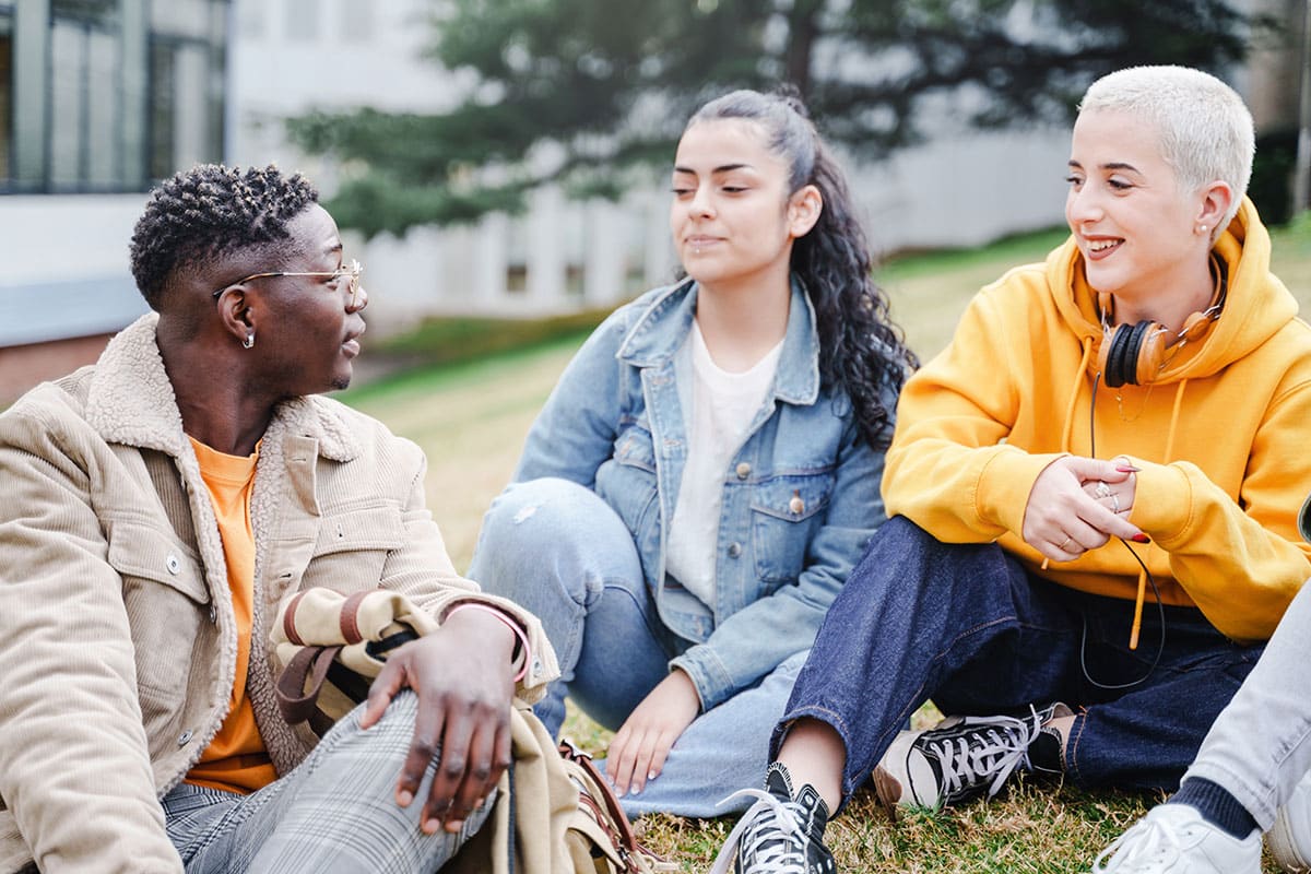 a group of three gen-z friends sit in a park listening to one persons excuses for cutting and self-harm