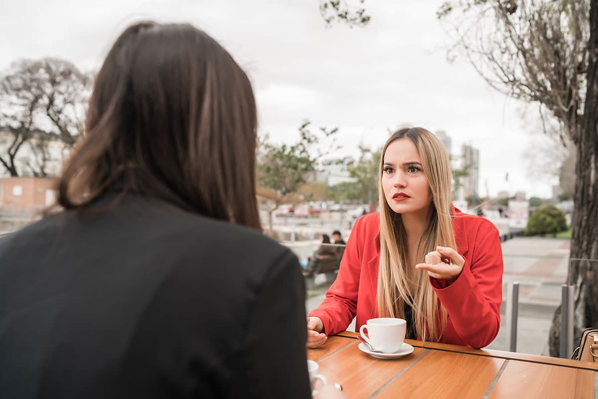 two young women sitting at a coffee table outside discussing life's problems