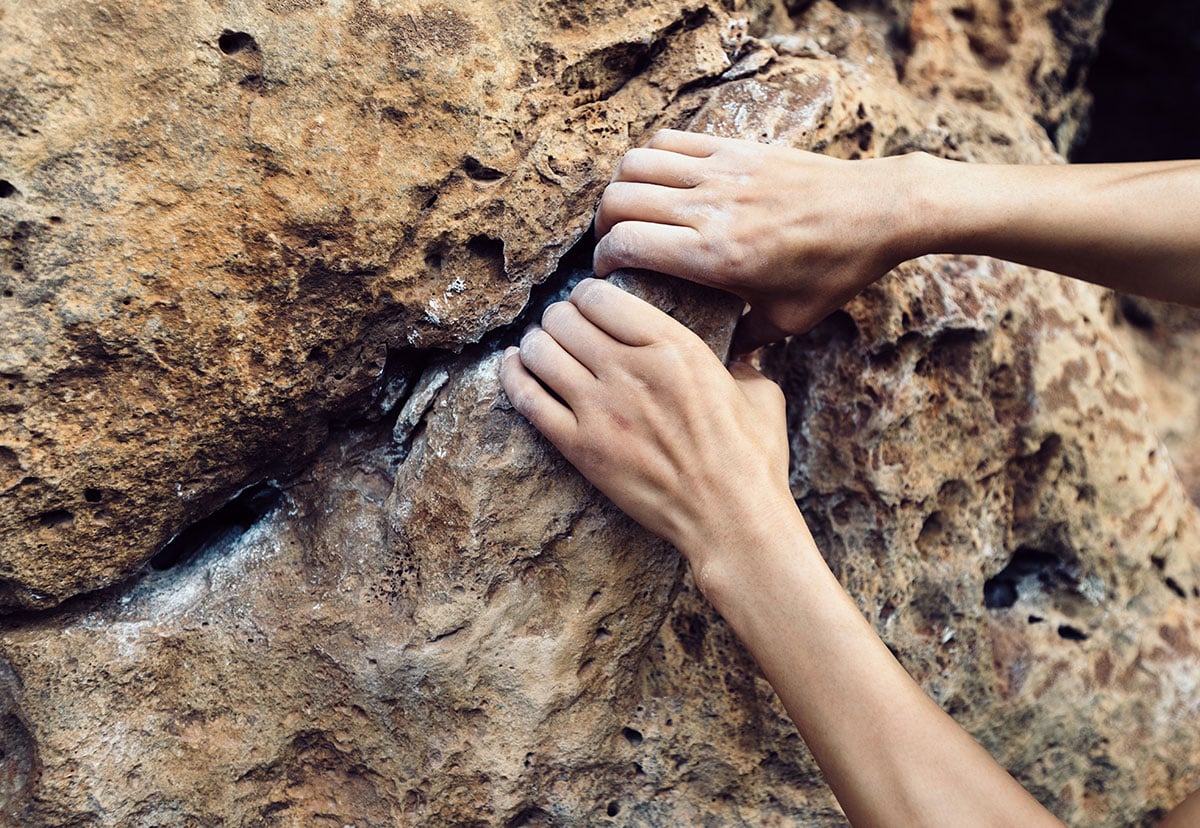 two chalky hands gripping onto some jagged rocks while rock climbing