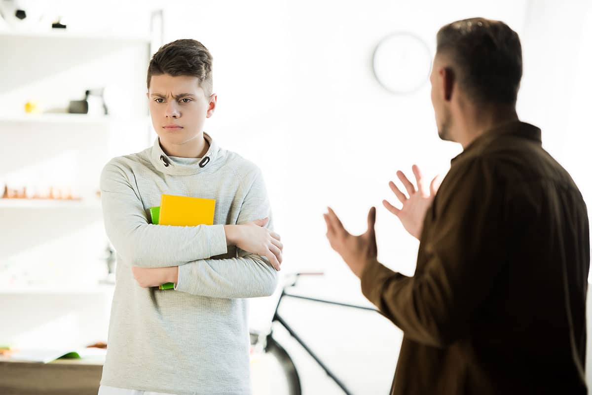 dad is yelling and gesturing at his sad looking son because he didn't give him good excuses to miss school