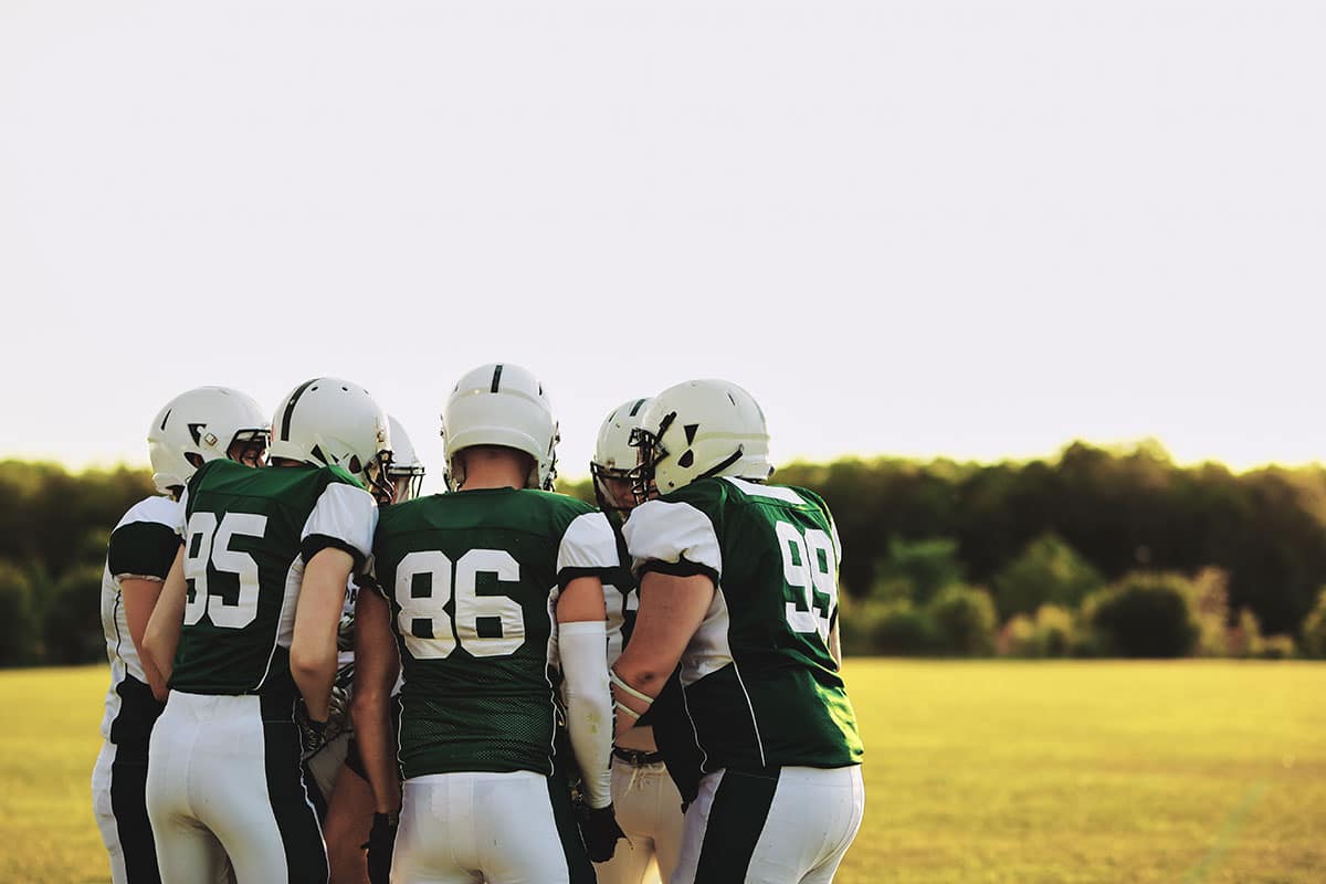 football team with good excuses to miss school in the huddle wearing green and white uniforms