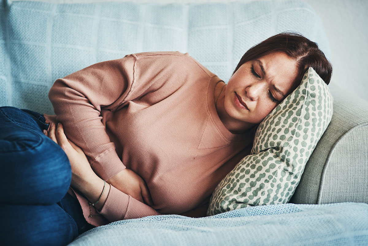 woman lying sideways on a couch holds her stomach because she ate too much food and is now using that as an excuse for not having sex