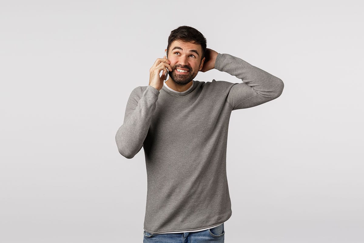 man in grey shirt rubs the back of his head as he is on the phone making excuses to get out plans