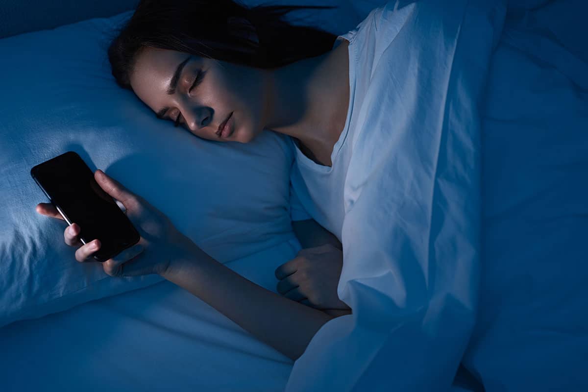 woman asleep in bed holding her smartphone in her hand