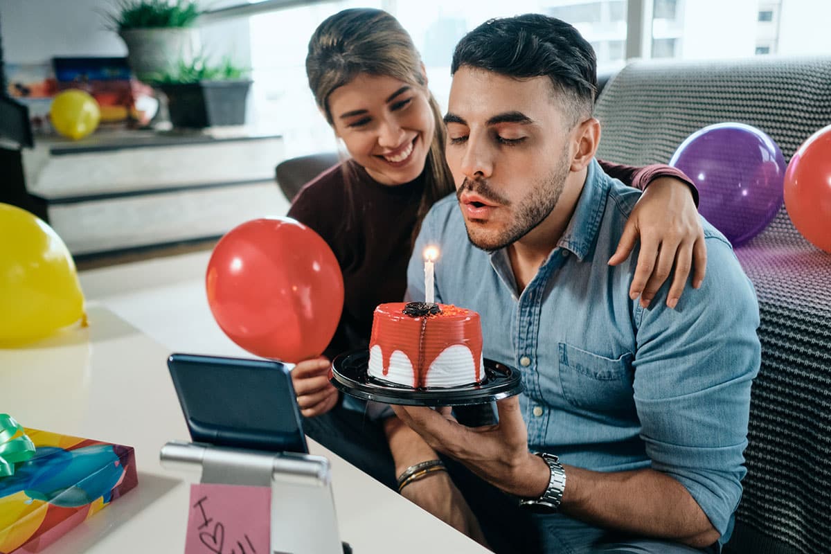 couple celebrating his birthday with a candle lit cake and balloons