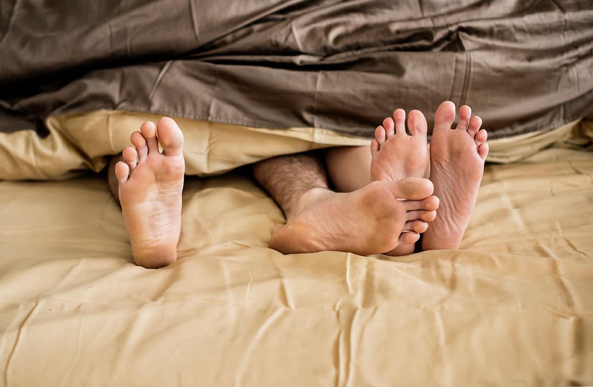 photo of couples feet touching as they stick out from under the bedsheets