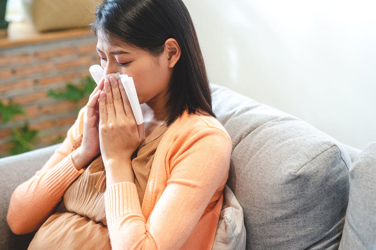 pregnant woman blowing her nose because she is sick