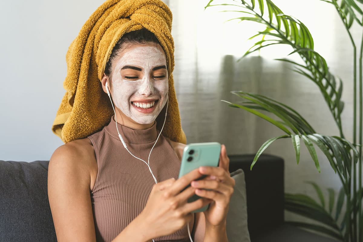 woman in the midst of her skincare routine with facemask and a phone in her hand