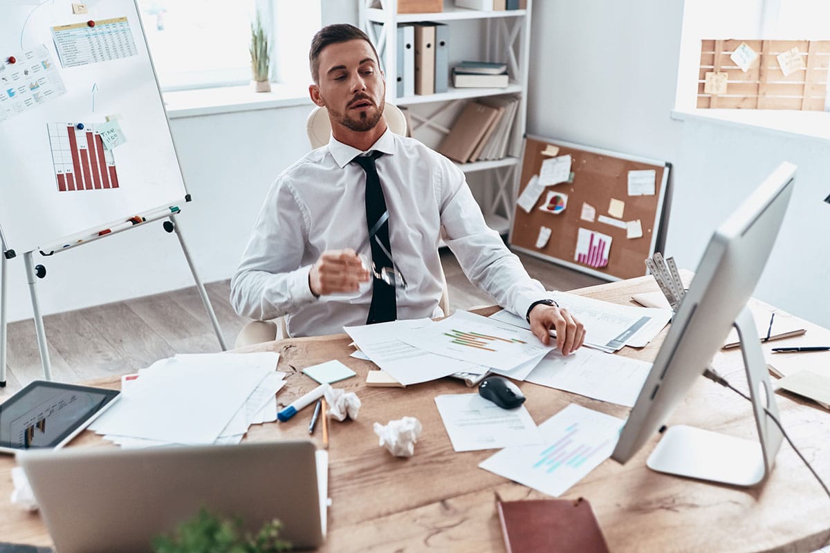 man looking tired as he's stuck in his office with lots of paperwork on his desk