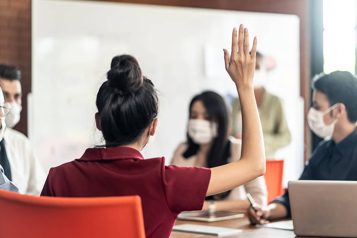 woman in work meeting raising her hand as she prepares an excuse to question authority