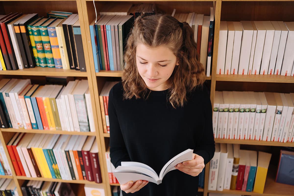 young girl in a black shirt reading through a book trying to find the answer to her questions