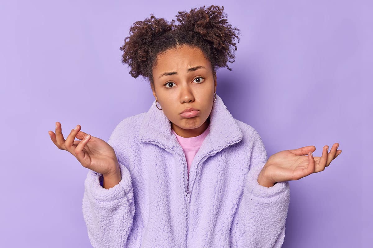 young woman on a purple background shrugs because she can't decide on something