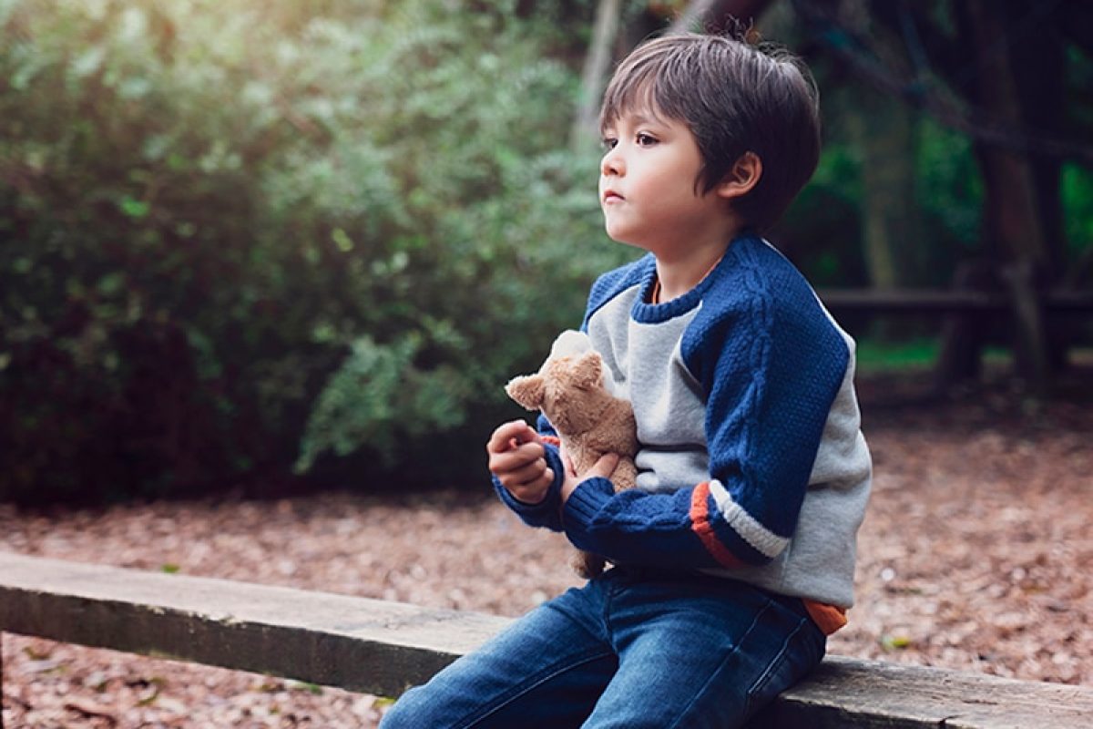 a lonely child sitting on a bench holding a stuffed animal