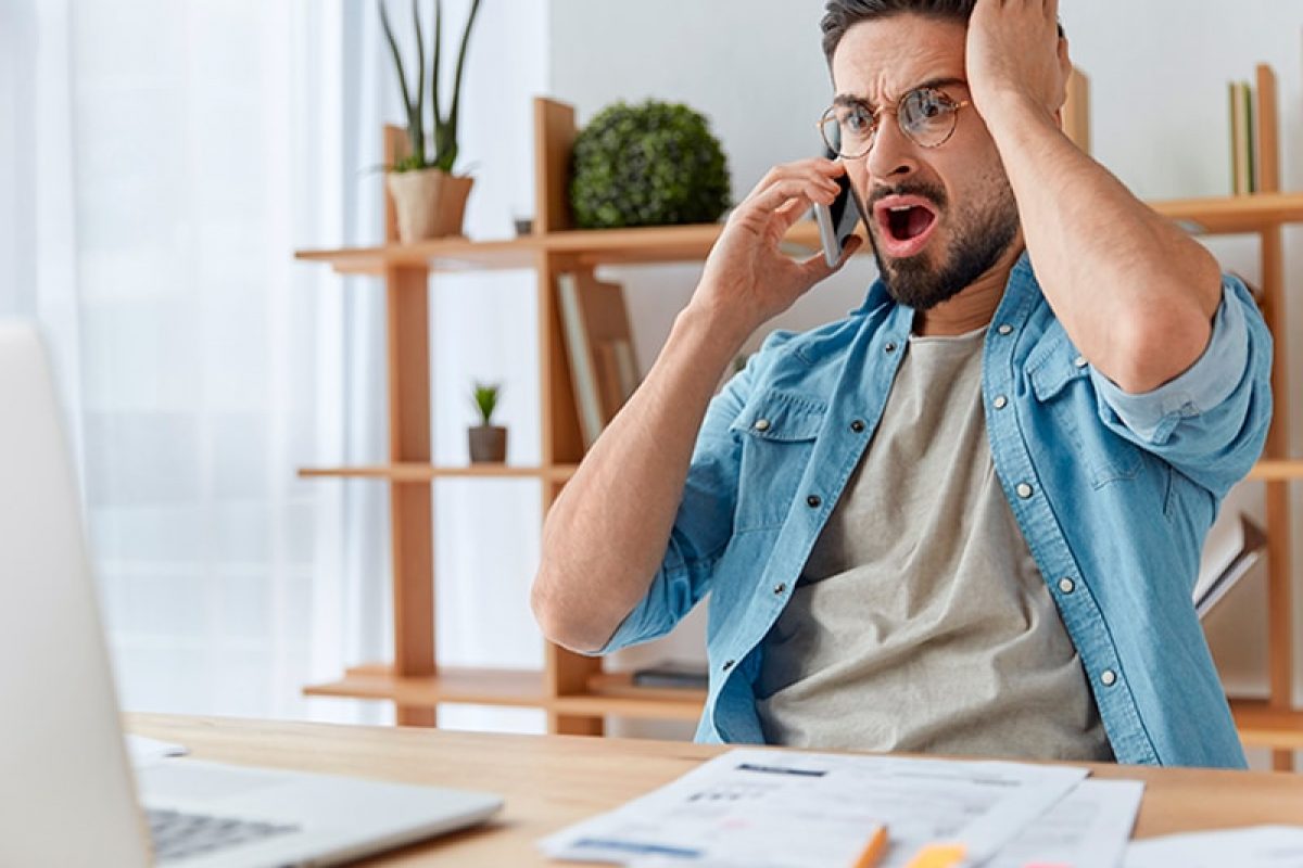 an upset man talking on the phone having a surprised reaction