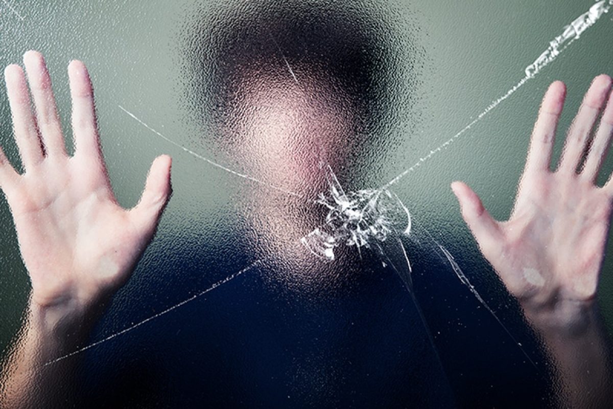 man holding his hands up against a broken window