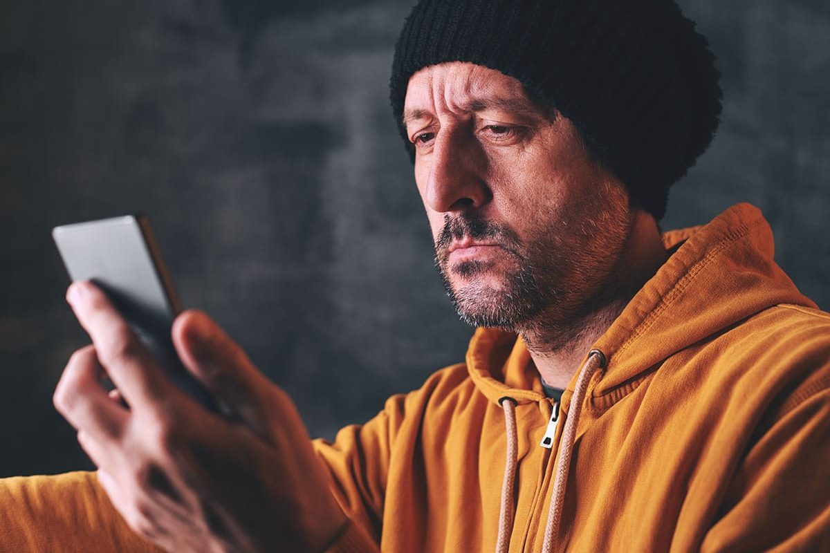 man in orange sweater and black beanie looking at sad with his phone