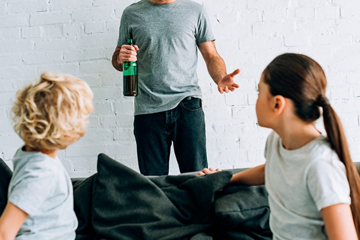 a man holding a bottle of wine talking to two women on a couch