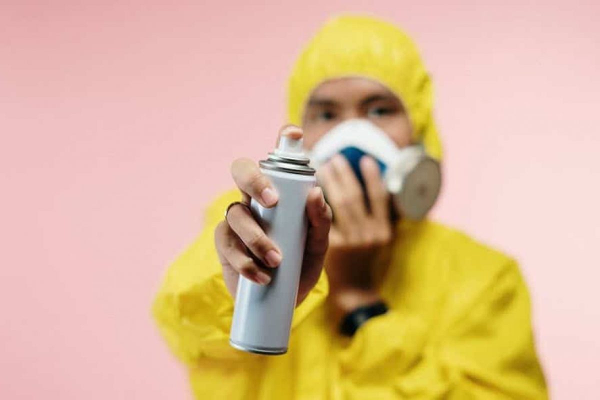 man in a yellow exterminator suit spraying an aerosol can