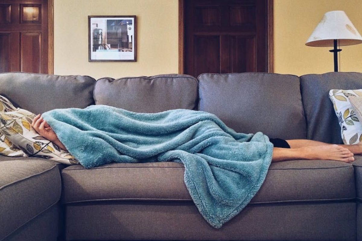 tired guy on couch with a blanket covering him